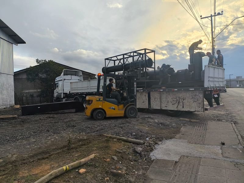 Empilhadeira descarregando equipamento pesado de um caminhão