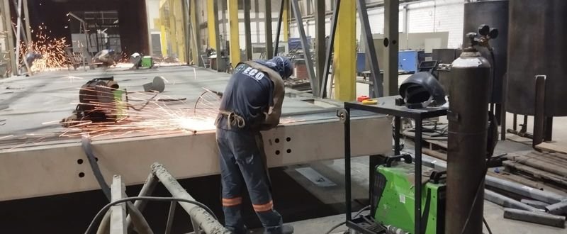 Soldador esmerilhando uma estrutura de aço, com faíscas